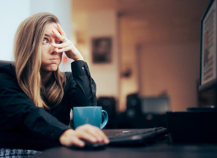 Woman stares at computer screen with one eye shut, indicating she is a content moderator viewing graphic content.