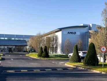 A large industrial building that is the AMD facility in Dublin. The front of the building and a large driveway with some trees and a blue sky are visible.