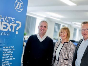 Two men and a woman stand next to each other with a poster on the left that has the ZF logo and reads "What's next?".