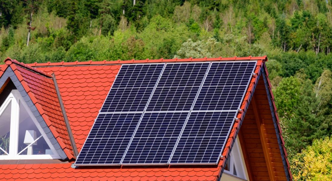 A house that has been retrofitted and has solar panels on the roof, with green trees behind it.