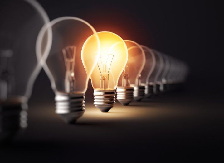 A row of lightbulbs with a single lightbulb lit up, in a dark room.