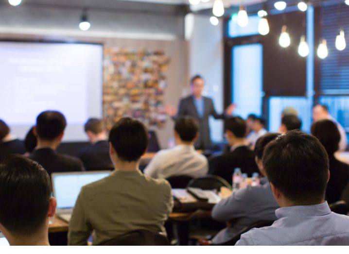 Person leading a business strategy meeting in a modern office room with a whiteboard and exposed red brick.