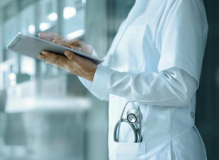A person in a medical outfit holding a tablet and typing on it, in a hospital hallway.
