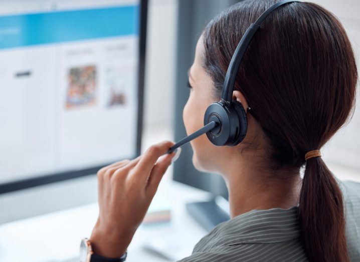 A woman speaking on a headset microphone while looking at a computer screen. Used to represent voice over internet protocol services.