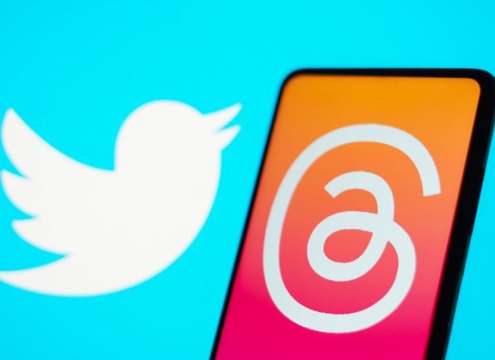 The Threads logo on a smartphone screen, with the Twitter logo in the background.