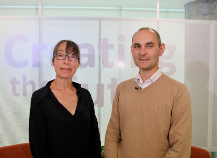 Ann O'Dea stands next to Prof Keane. She is wearing black and he has a white shirt and camel jumper on. The creating the future sign is behind them.