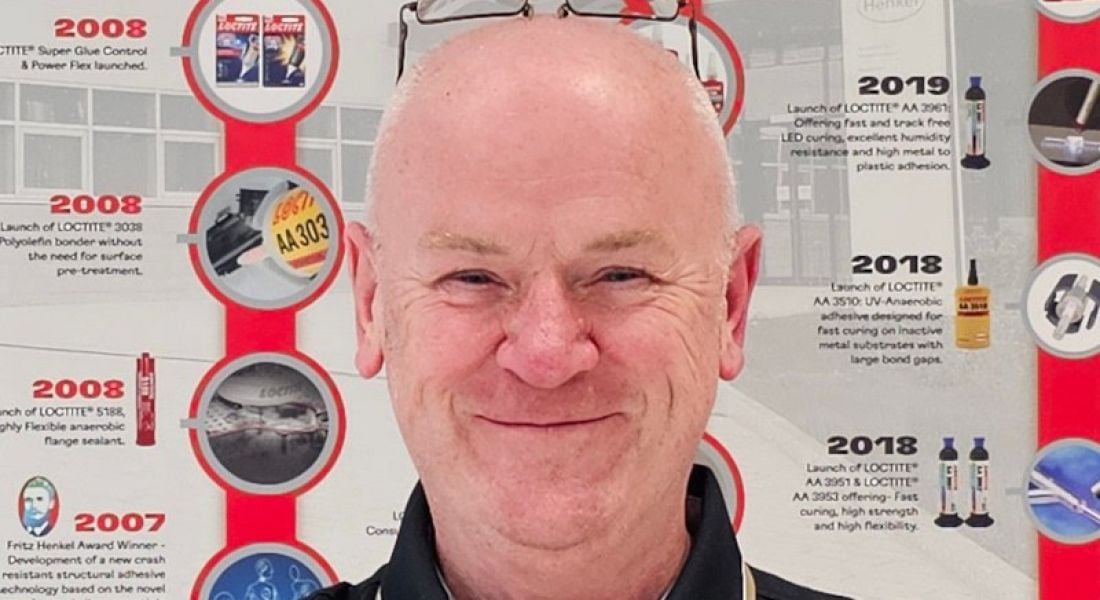A man smiles while standing in front of an information board. He is Barry Burns, a technical lead at Henkel.