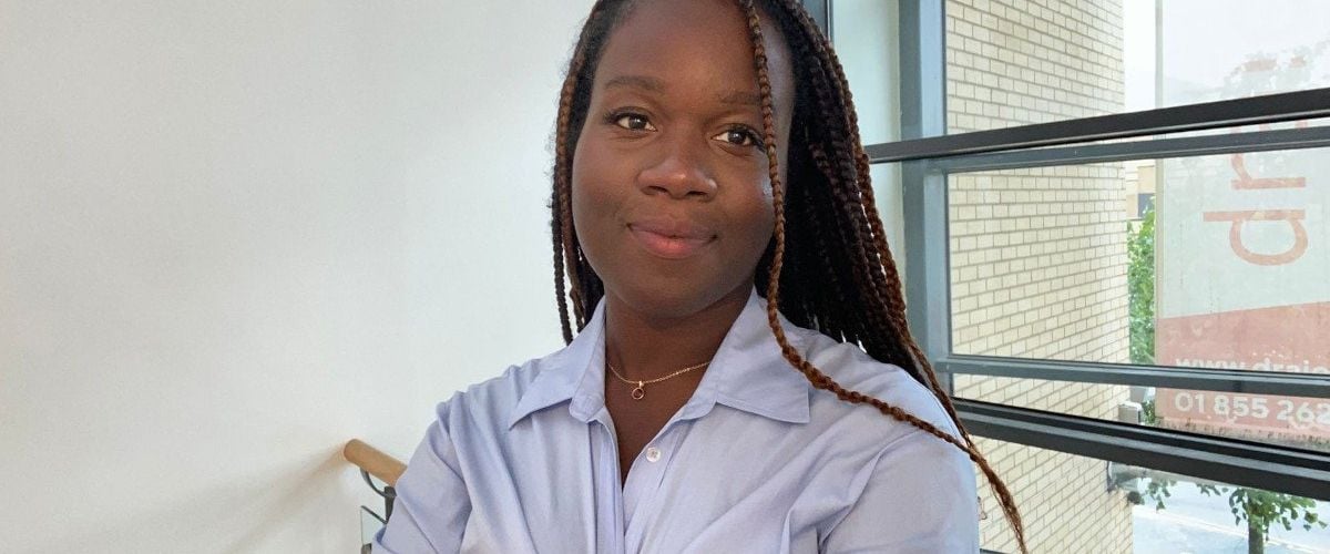 A woman wearing a light blue shirt smiles with her arms crossed in an office setting. She is Blessing Folayan, a radiographer and technology consulting analyst at Deloitte.