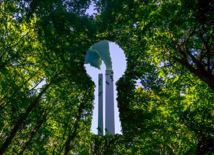 From a forest floor looking up to a key shaped hole in the leaves and two chimney stacks billowing smoke visible to show greenwashing concept.
