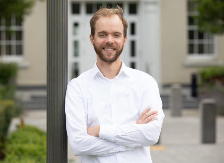 A man wearing a white shirt smiles as he leans against a pole with a building behind him. He is James Hogan, co-founder and CTO at Bundledocs.