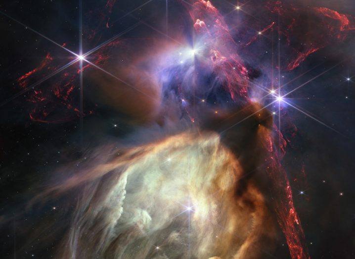 A cloud complex in space, showing different gas clouds of different colours clashing together in space, with multiple stars visible across the image.