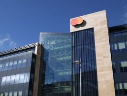 A man stands in front of a wall with the Mastercard logo on it. He is Ngoc Minh Tran, a lead data scientist at Mastercard.