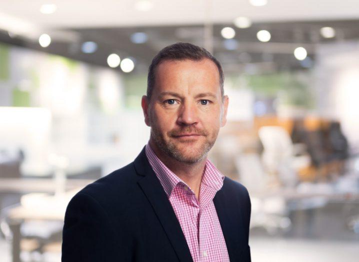 A man wearing a suit with a pink shirt smiles at the camera with an office setting behind him. He is Mervyn O'Callaghan, CEO of CameraMatics.