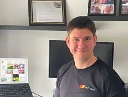 A man stands in front of a wall with the Mastercard logo on it. He is Ngoc Minh Tran, a lead data scientist at Mastercard.