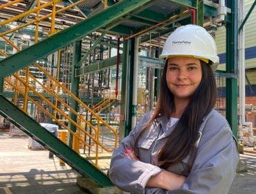 A woman wearing a hard hat smiles at the camera in an industrial site. She is Sarah Kelly, an engineer at Thermo Fisher Scientific.