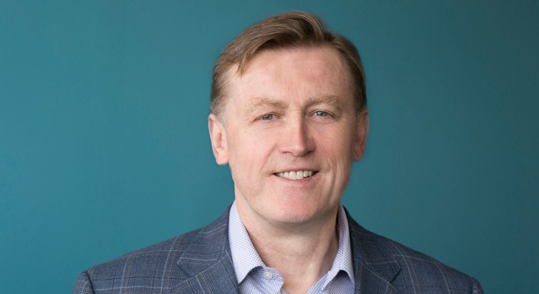 Headshot of a man in a grey suit, with a green-blue background. He is Vincent Roche of Analog Devices.