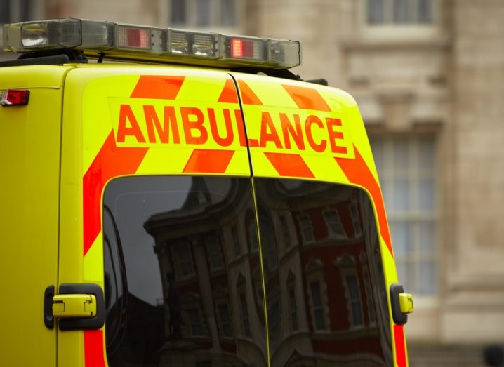 Rear view of a yellow and orange ambulance in front of a sandstone building.