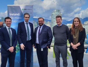 Four men and one woman stand outdoors in front of an IDA Ireland banner smiling at the camera.