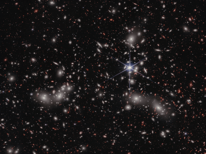 James Webb image of thousands of galaxies in Pandora’s Cluster. Many little colourful dots and arcs can be seen across the darkness of the universe.